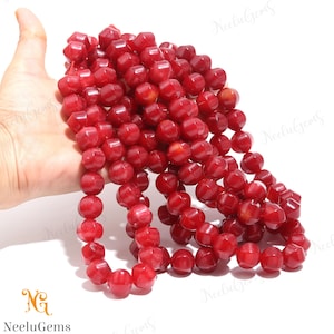 May include: Strand of faceted, deep red gemstone beads. The beads are a rich, saturated color and have a geometric, rounded shape. The beads are strung together, creating a necklace or strand for jewelry making. The logo "Neelu Gems" is in the bottom left corner.
