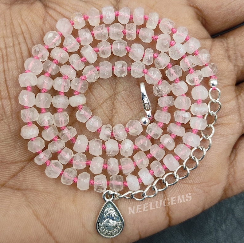 May include: A pink string necklace with faceted clear quartz beads and a silver charm with the text "NEELUGEMS".