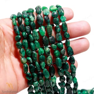 May include: A strand of green gemstone beads, each bead is a smooth, oval shape with a slightly irregular surface. The beads are strung together on a clear thread.