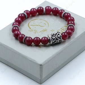 May include: A red gemstone bracelet with silver beads and a silver charm. The bracelet is in a white box with the text "N.G. Gems" on it.