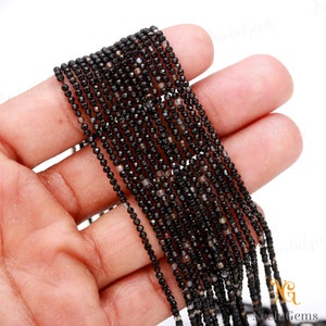 May include: A strand of black faceted gemstone beads. The beads are small and round, and they are strung on a thin wire. The beads are arranged in a straight line, and they are all the same size and shape.