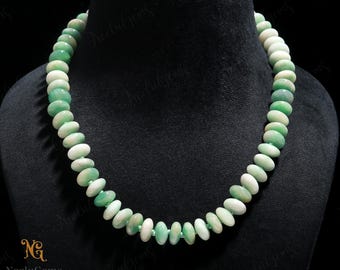 May include: A beaded necklace featuring alternating green and white oval-shaped beads. The necklace is displayed on a black mannequin. The beads are strung together, creating a smooth, elegant design. The necklace is a piece of jewelry.