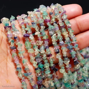 May include: A strand of multi-colored chip beads. The beads are a mix of green, blue, purple, and pink. The beads are small and irregular in shape. The beads are strung on a clear thread.