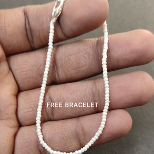 May include: A white beaded bracelet with a silver clasp. The bracelet is on a person's hand. "FREE BRACELET" is written on the hand.