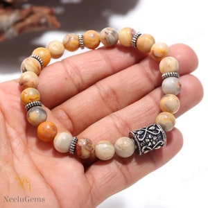May include: A bracelet made of brown and white agate beads with silver accents. The bracelet has a silver charm with a floral design.
