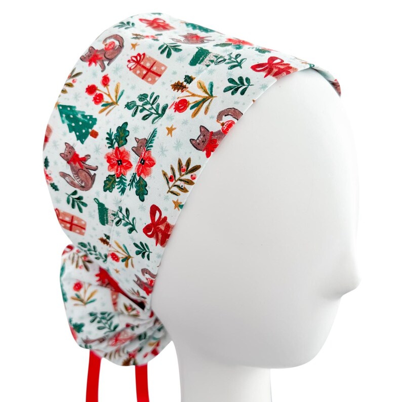 May include: A white scrub cap featuring a Christmas-themed pattern. The design includes red foxes, gift boxes, Christmas trees, and floral accents. The cap has red ties and is displayed on a mannequin head.