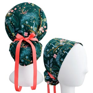 May include: A dark green scrub cap featuring a botanical print with peacocks, branches, and pink flowers. The cap includes a bright coral ribbon tied in a bow at the back, with long trailing ends, designed to secure the fabric over the head.