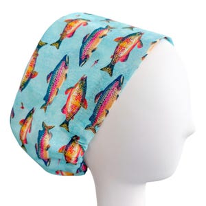 May include: A light blue scrub cap featuring a repeating pattern of colorful rainbow trout. The fish have vibrant hues of pink, orange, yellow, and blue. The cap is made of a soft fabric and is designed to fit comfortably.