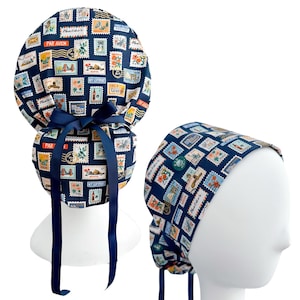 May include: Navy blue scrub cap with a repeating pattern of colorful postage stamps. The cap features a dark blue bow and ties. A second cap is shown on a mannequin head.