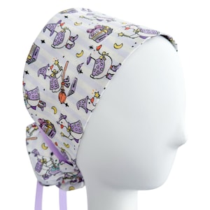 May include: A white scrub cap with a repeating pattern of cartoon witch characters, stars, moons, and spell books. The cap has a purple striped background and purple ties.