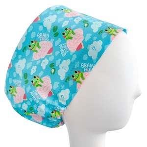 May include: A light blue scrub cap featuring a repeating pattern of cartoon frogs with pink brains, white clouds, and question marks. The words "BRAIN FROG" are printed on the cap. The cap is designed to fit the head.