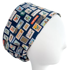 May include: A navy blue scrub cap featuring a repeating pattern of colorful postage stamps. The stamps include images of flowers, landmarks, and text such as "PAR AVION" and "SPAIN". The cap is designed to fit comfortably and securely.