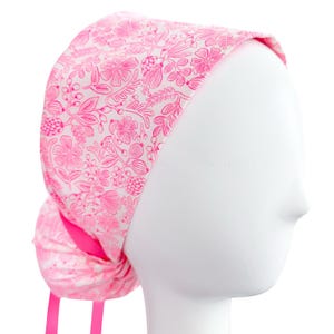 May include: A pink and white surgical scrub hat with a floral pattern. The hat has a tie at the back.