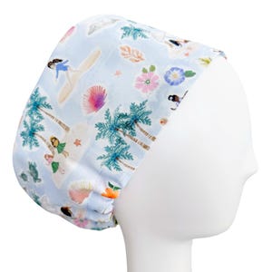 May include: A light blue surgical scrub cap featuring a tropical beach scene. The cap is adorned with palm trees, surfers, seashells, and flowers in shades of pink, green, and orange. The cap is designed to fit comfortably and securely.
