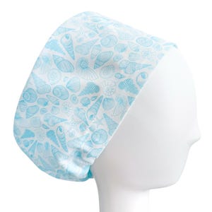 May include: A white and light blue patterned scrub cap featuring a seashell design. The cap is made of a soft fabric and is designed to fit comfortably. The light blue seashells are in various shapes and sizes.