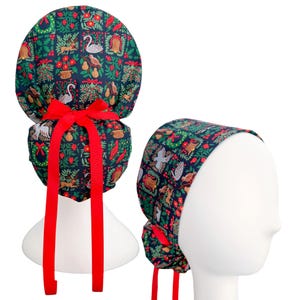 May include: A dark blue scrub cap featuring a repeating pattern of Christmas-themed illustrations including swans, pears, wreaths, and birds. The cap includes a bright red ribbon tie at the back, designed to secure the fabric in a gathered style.