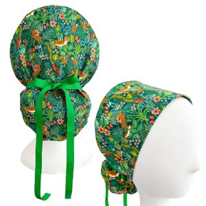 May include: A green scrub cap with a jungle-themed pattern featuring tigers, flowers, and foliage. The cap has a ponytail design and is tied with a green ribbon. The cap is shown on a white mannequin head.