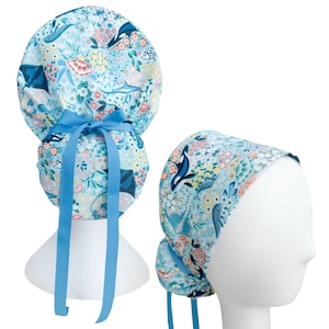 May include: A light blue surgical scrub cap with a marine life pattern, including whales, stingrays, and floral elements. The cap has a matching blue ribbon for tying. The second image shows the cap on a mannequin head.