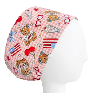 May include: A pink and white checkered scrub cap featuring a repeating pattern of teddy bears, American flags, cherries, milkshakes, and heart-shaped sunglasses. The bears wear shirts with the American flag design. The cap is on a white mannequin head.