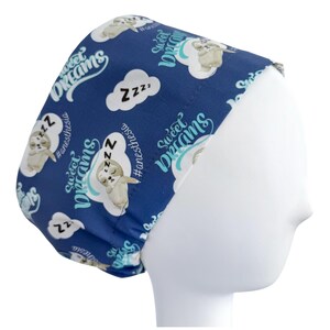 May include: A navy blue scrub cap featuring a repeating pattern of sleeping sloths, clouds, and the words "Sweet Dreams" and "#anesthesia" in white and teal. The cap is designed to fit comfortably and securely.