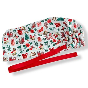 May include: A white scrub cap with a festive Christmas pattern featuring squirrels, gifts, and Christmas trees in red, green, and brown. The cap has a red ribbon attached for tying.