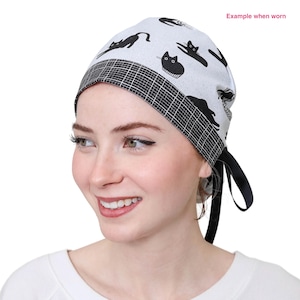 May include: A white surgical scrub cap featuring a black cat design. The cap has a black and white chequered border and black ties. The text "Example when worn" is visible in the upper right corner.