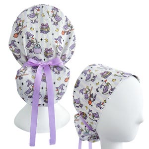 May include: A white scrub cap with a repeating pattern of purple witch ducks, moons, stars, and spell books. The cap has a lavender ribbon and is displayed on a mannequin head. The second image shows a close-up of the cap.