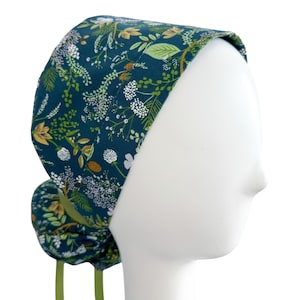 May include: A teal blue surgical scrub hat with a floral pattern featuring white, green, and yellow flowers. The hat has a gathered back and green ties.