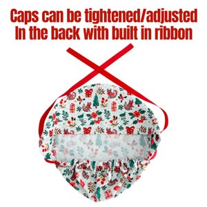 May include: A white patterned cap with a festive design featuring foxes, Christmas trees, and gifts. The cap has a red ribbon for adjustment and the text "Caps can be tightened/adjusted In the back with built in ribbon".