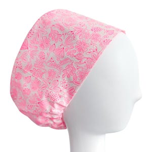 May include: A pink floral patterned scrub cap. The cap features a repeating design of flowers, leaves, and berries in a bright pink color against a white background. The cap is designed to fit snugly around the head.