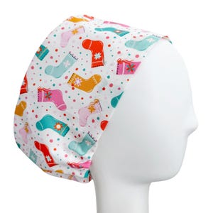 May include: A white scrub cap featuring a repeating pattern of colorful Christmas stockings in shades of red, teal, pink, and yellow, accented with small multicolored polka dots throughout the fabric design on a white background.
