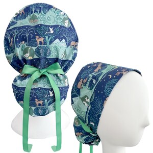 May include: A scrub cap with a forest animal print in shades of blue and green. The cap features a green bow and ties. The design includes deer, rabbits, and trees. The cap is designed to be worn on the head.