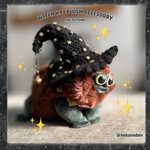 Pode incluir: Um brinquedo de pelúcia em forma de criatura usando um chapéu de bruxa preto adornado com estrelas douradas. O brinquedo tem olhos grandes e expressivos e um corpo peludo marrom-avermelhado. O texto "WITCH HAT PLUSH ACCESSORY PDF PATTERN" é visível.