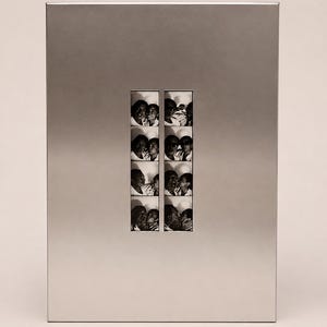 Puede incluir: Un marco rectangular de metal plateado con un recorte vertical central que muestra dos tiras paralelas de fotografías en blanco y negro de fotomatón. Cada tira contiene cuatro cuadros individuales que muestran a dos personas interactuando de cerca.