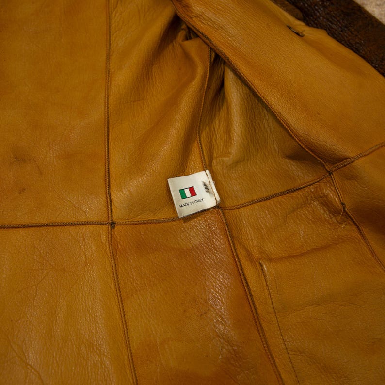 May include: Close-up of the interior of a brown leather jacket. The lining is a lighter shade of brown. A tag with the Italian flag and the words "MADE IN ITALY" is visible.