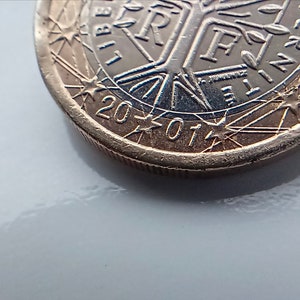 May include: Close-up of a gold-coloured 2001 Euro coin with the inscription "LIBERTE EGALITE FRATERNITE" and a tree design. The coin is on a white surface.