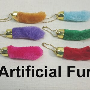 May include: Five faux fur keychains in different colors: orange, purple, green, pink, and red. Each keychain has a gold metal ring and a chain.