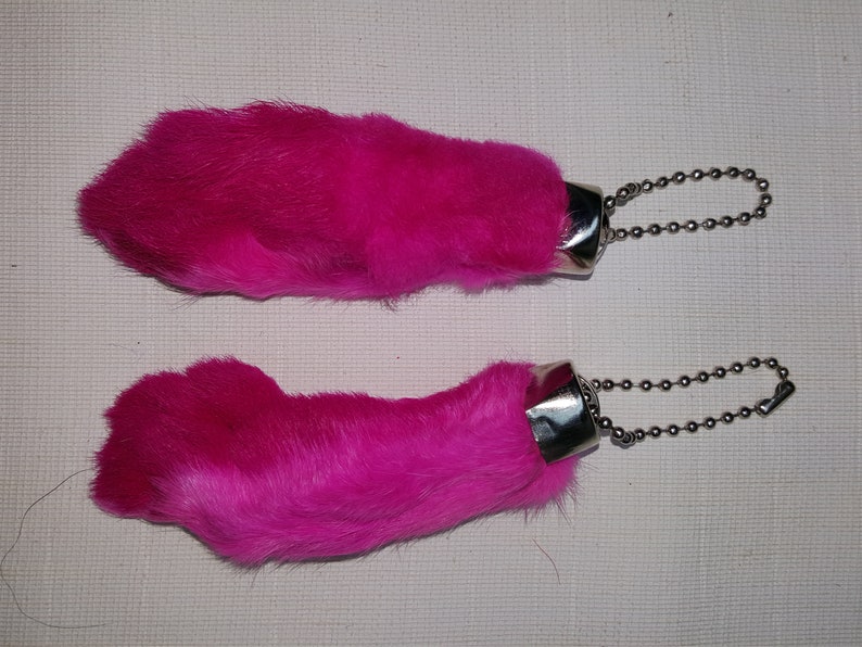 May include: Two pink fuzzy rabbit foot keychains with silver metal rings and chains.