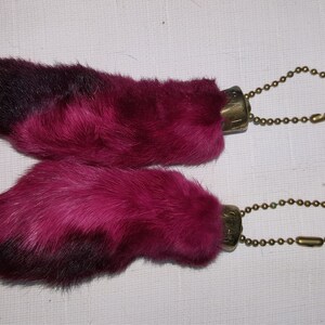 May include: Two pink rabbit foot keychains with gold chains. The rabbit feet are made of fur and have black tips.