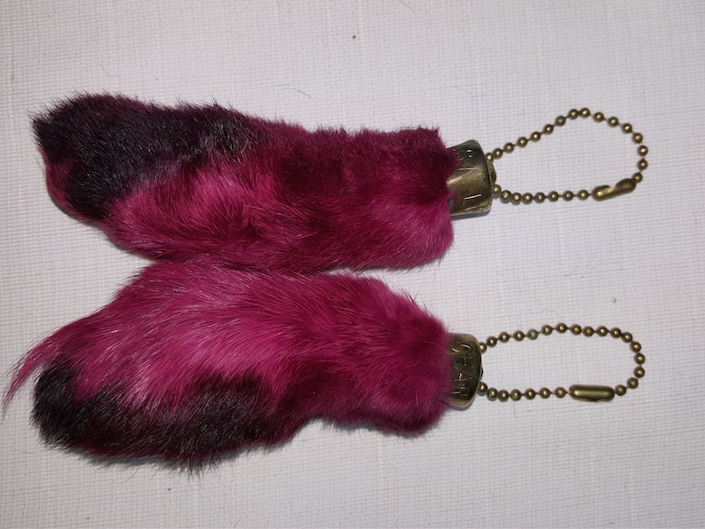 May include: Two pink rabbit foot keychains with gold chains. The rabbit feet are made of fur and have black tips.