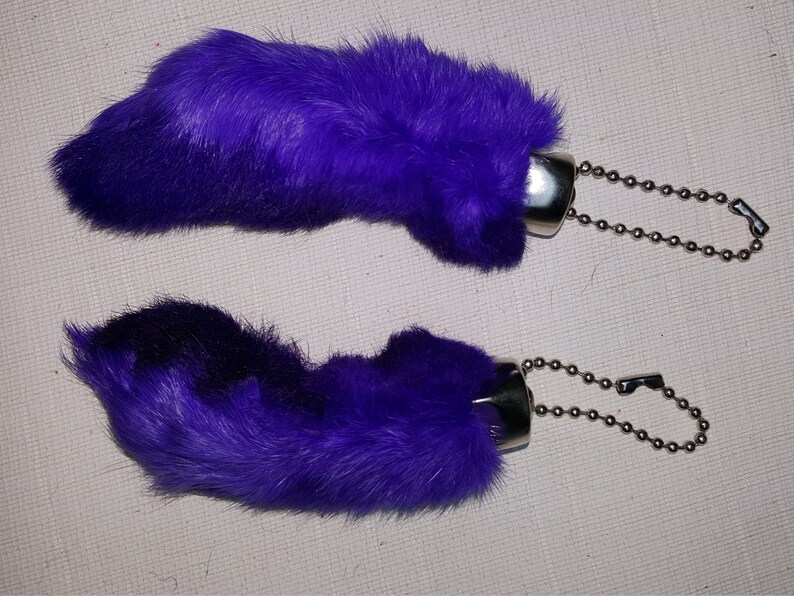 May include: Two purple faux fur rabbit foot keychains with silver metal rings and chains.