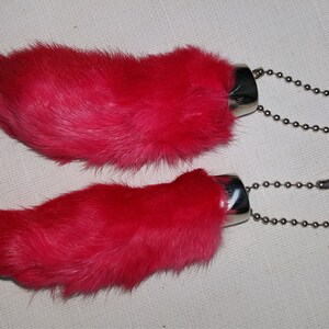 May include: Two pink rabbit foot keychains with silver metal rings and chains. The rabbit feet are made of fur.