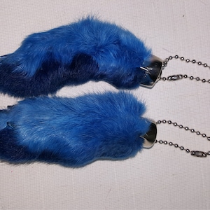May include: Two blue rabbit foot keychains with silver metal rings and chains.