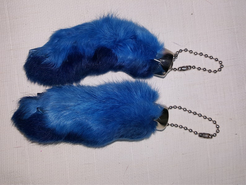 May include: Two blue rabbit foot keychains with silver metal rings and chains.