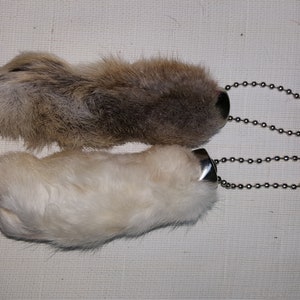 May include: Two rabbit foot keychains with silver chains. The top keychain has a brown rabbit foot and the bottom keychain has a white rabbit foot.