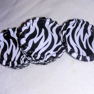 May include: Three black and white zebra print bottle caps. The caps are stacked on top of each other.