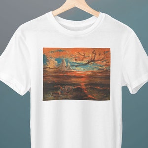 May include: A white t-shirt with a print of a painting of a sunset over a body of water. The sky is a mix of orange, red, and blue with clouds. The water is a dark blue with a few white waves.