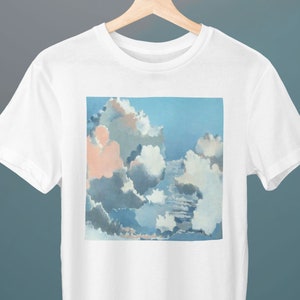 Könnte beinhalten: Weißes T-Shirt mit einem Grafikdruck eines blauen und rosafarbenen Himmels mit flauschigen weißen Wolken.