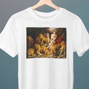 May include: White t-shirt with a print of a painting depicting a man surrounded by lions in a dark forest setting.