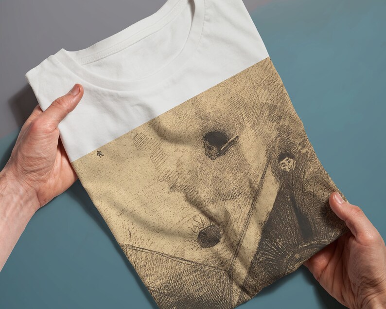 May include: A white t-shirt with a vintage-style drawing of a person in a hat and a cloak. The drawing is in shades of brown and beige.